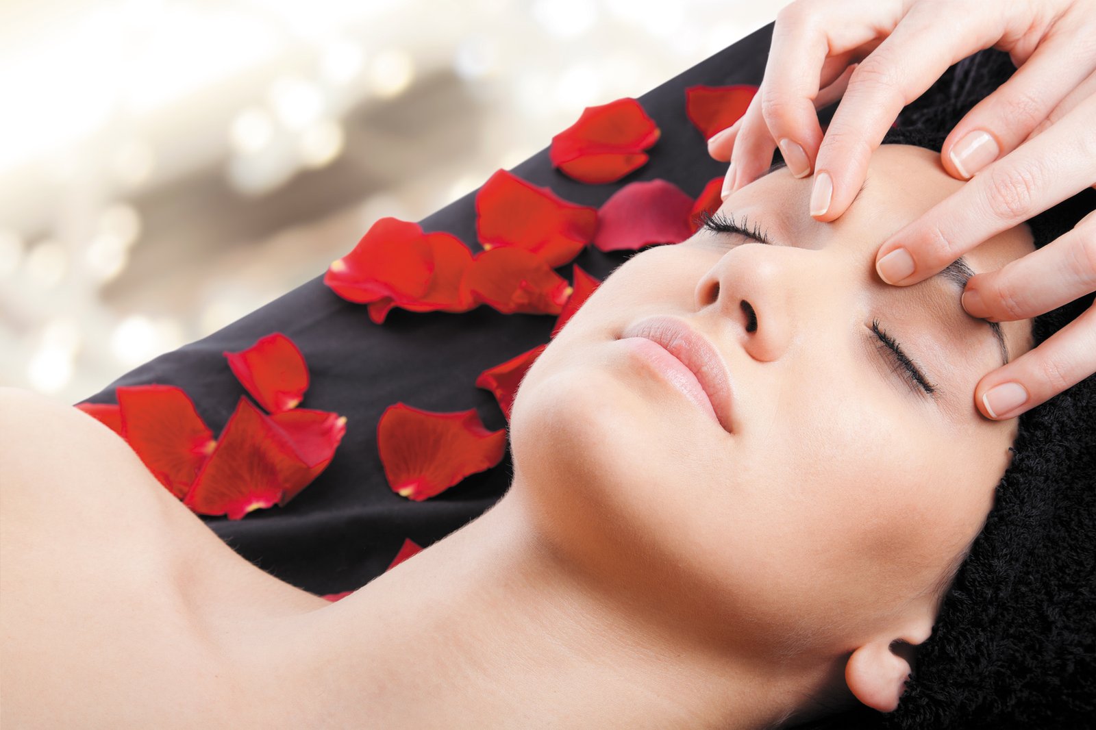 Beautiful woman receiving a facial massage lying on bed with rose petals.